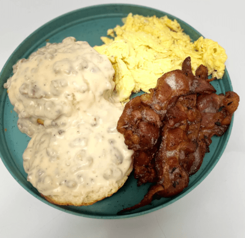 A plate with biscuits and sausage gravy, scrambled eggs, and crispy bacon.