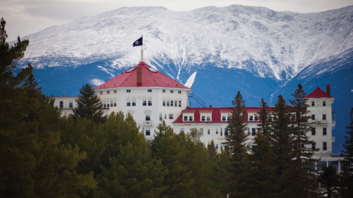 Historic hotel with a red roof, surrounded by trees, set against a backdrop of snow-capped mountains.