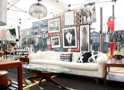 A stylish outdoor display featuring a white sofa, art prints, and decorative items under a tent.
