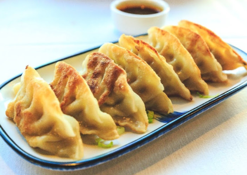 A plate of golden-brown dumplings arranged neatly, served with a small bowl of dipping sauce.