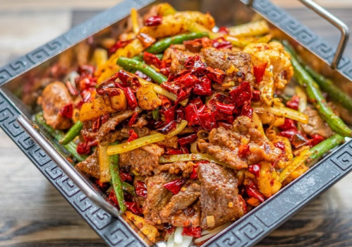 A metal dish filled with spicy stir-fried meat and vegetables, garnished with red chili peppers.
