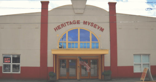 Front view of the Heritage Museum building, featuring large windows and an American flag, with a gift shop sign visible.