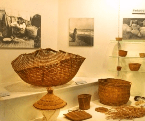 Display of woven baskets and artifacts in a museum, with historical photos in the background.