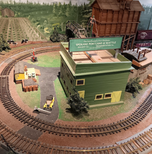 Model train layout featuring a green building labeled "Spokane Portland & Seattle" with tracks and miniature scenery.