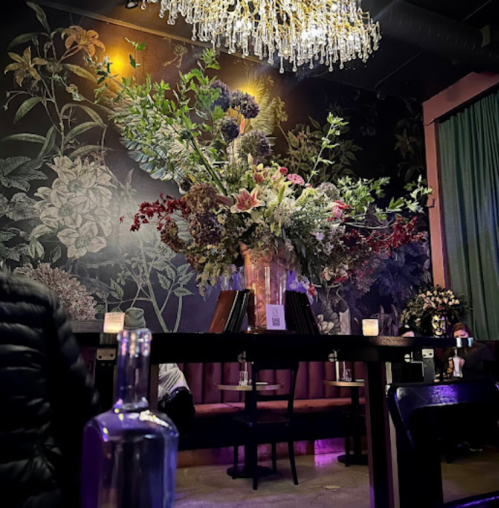 A stylish interior featuring a large floral arrangement under a chandelier, with dim lighting and elegant decor.