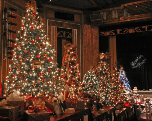 A festive display of decorated Christmas trees with lights and ornaments in a theater setting.