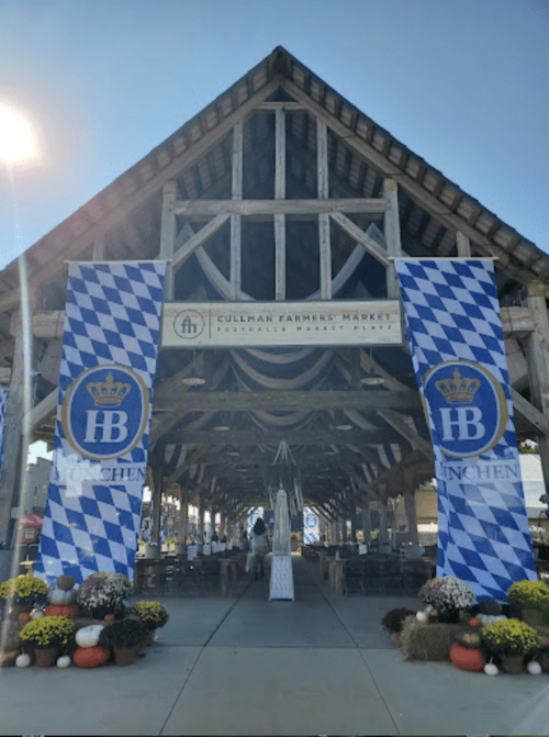 Entrance to Cullman Farmers Market, featuring blue and white banners and decorative flowers. Bright, sunny day.