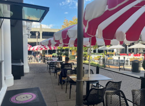 Outdoor dining area with red and white striped umbrellas, tables, and a clear blue sky in the background.