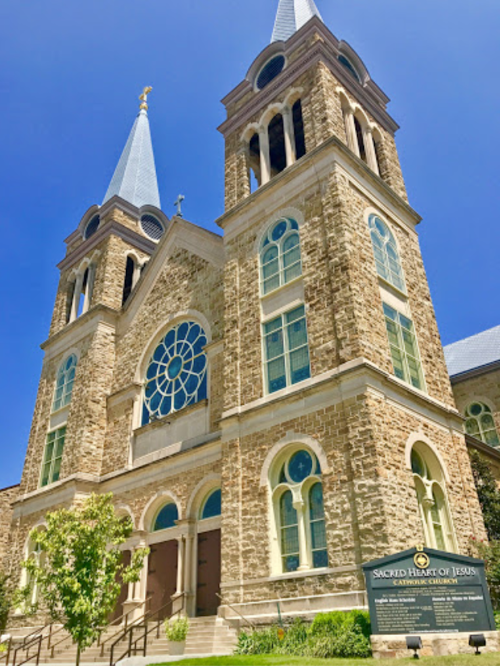 Historic stone church with tall spires, large stained glass window, and a sign for Sacred Heart of Jesus Catholic Church.