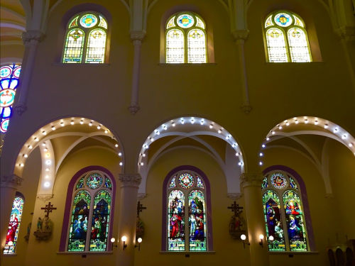 Colorful stained glass windows in a church, featuring intricate designs and vibrant light filtering through.