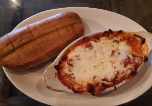 A baked dish with melted cheese and sauce, served alongside a sliced loaf of bread on a white plate.