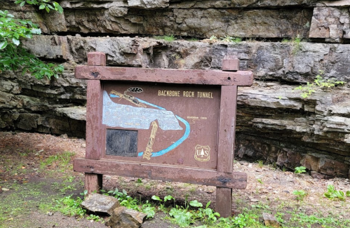 Sign for Backbone Rock Tunnel, featuring a map and information about the tunnel, set against a rocky background.
