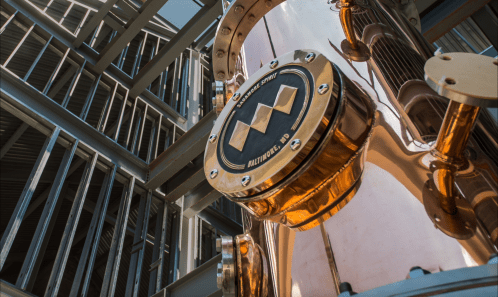 Close-up of a shiny copper distillation apparatus against a modern industrial backdrop.