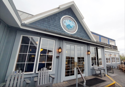 Exterior of Nick's restaurant featuring a blue shingle facade, large windows, and wooden seating outside.
