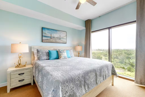 Bright bedroom with a large bed, decorative pillows, two lamps, and a scenic window view.