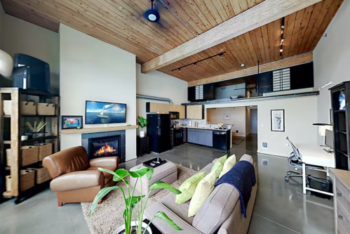 Spacious modern apartment with wooden beams, a cozy fireplace, and a stylish living area featuring a sofa and desk.