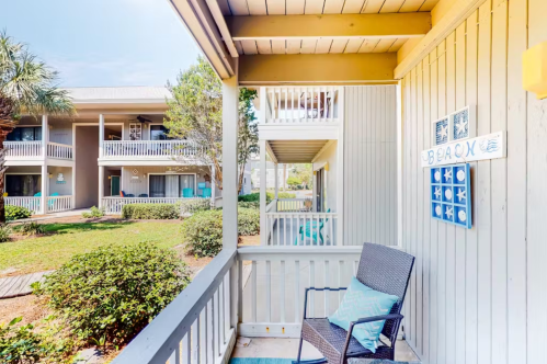 A cozy balcony with a chair overlooks a landscaped courtyard and nearby buildings in a beachside setting.