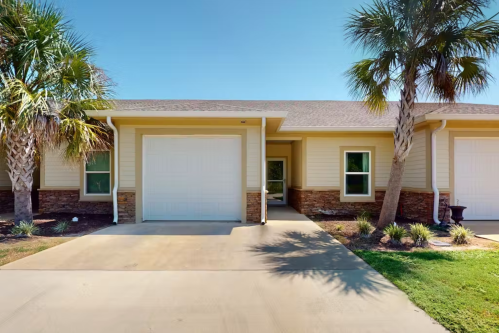 A single-story home with a garage, palm trees, and a landscaped front yard.