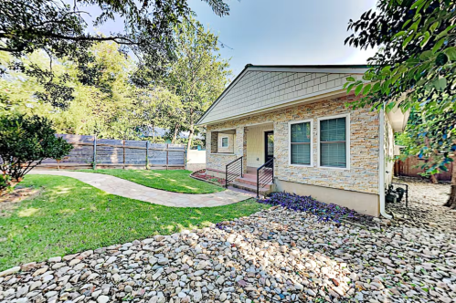 A charming house with a stone pathway, surrounded by greenery and a landscaped yard.