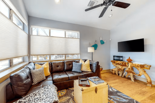 Cozy living room with a brown leather sofa, decorative pillows, a wooden table, and a TV on the wall.