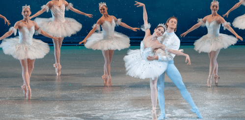 A ballet performance featuring dancers in white tutus, with a couple in the foreground striking a graceful pose.