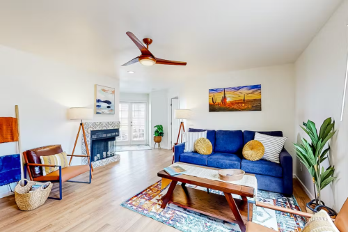 Cozy living room with a blue sofa, wooden coffee table, plants, and a ceiling fan, featuring warm decor and natural light.