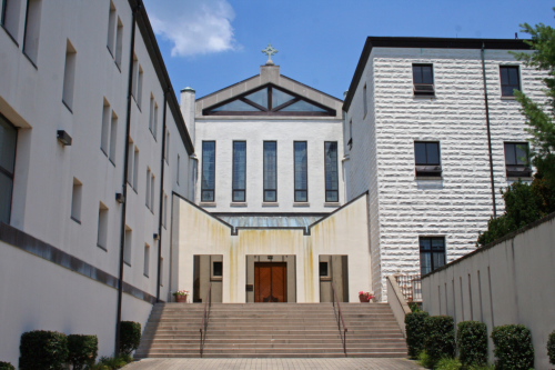 A modern church building with a cross on top, flanked by two white structures and a staircase leading to the entrance.