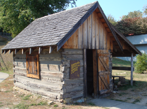 A rustic wooden cabin with a sloped roof, featuring a sign that reads "Knight's Forge" and a wooden door.