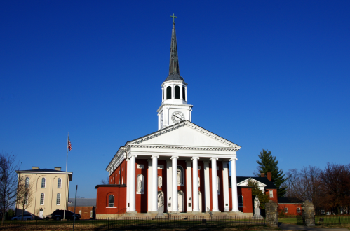 A historic church with a tall steeple, white columns, and a clock, set against a clear blue sky.