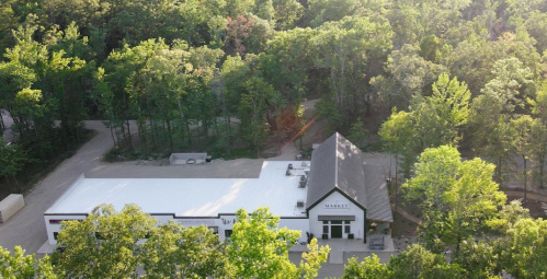 Aerial view of a building surrounded by lush green trees, featuring a white roof and large windows.