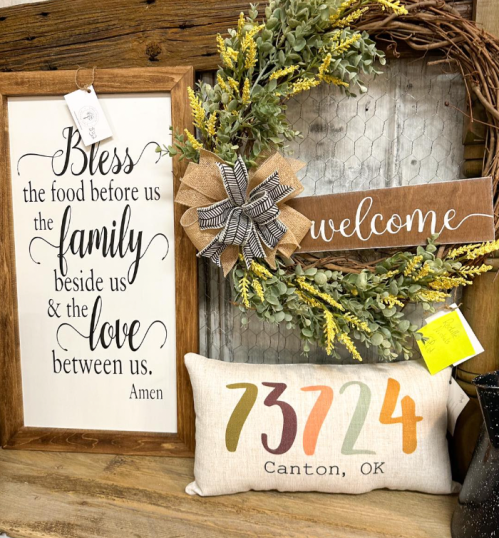 A decorative display featuring a sign with a blessing, a welcome sign, and a pillow with "73724 Canton, OK" printed on it.