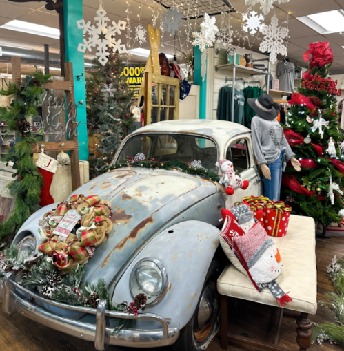 A vintage car decorated for Christmas, surrounded by festive decor, including a mannequin and holiday decorations.
