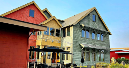 A colorful multi-story building with outdoor seating, surrounded by greenery and clear blue skies.