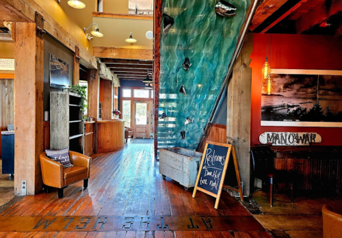 Interior of a rustic restaurant featuring wooden beams, a rock climbing wall, and a welcoming atmosphere.