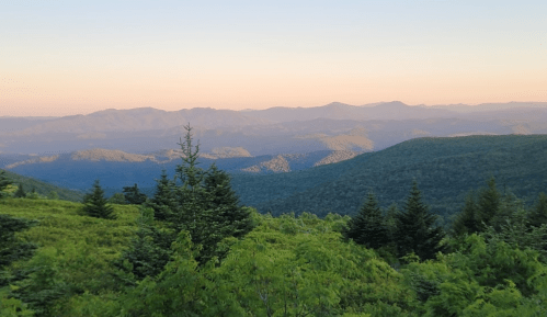 A scenic view of rolling mountains and lush greenery under a soft sunset sky.