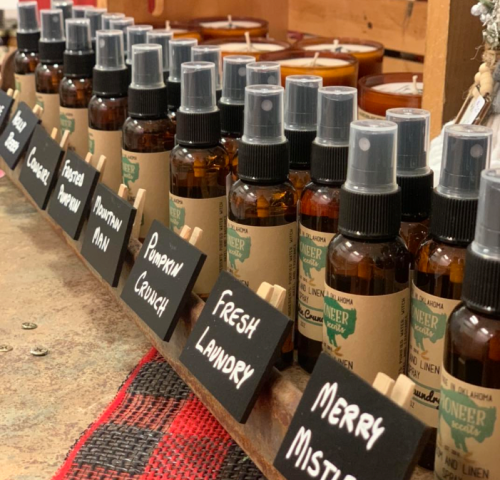 A display of various scented spray bottles and candles, each labeled with unique fragrance names.