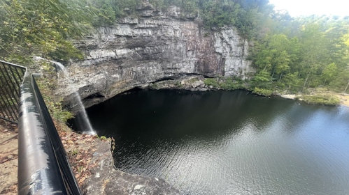 A scenic view of a waterfall cascading into a dark pool, surrounded by rocky cliffs and lush greenery.
