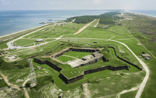 Aerial view of a star-shaped fort surrounded by green fields and a coastline in the background.