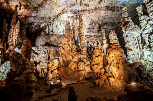 Stalactites and stalagmites in a dimly lit cave, showcasing intricate rock formations and textures.