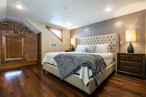Cozy bedroom featuring a large bed, wooden floors, brick wall accents, and stylish lamps on nightstands.
