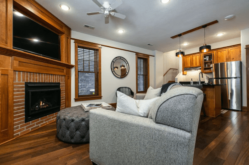 Cozy living room with a fireplace, modern kitchen, and stylish furniture, featuring wooden accents and warm lighting.