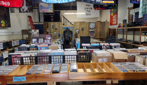 A spacious record store filled with shelves of vinyl records and CDs, decorated with colorful banners and posters.