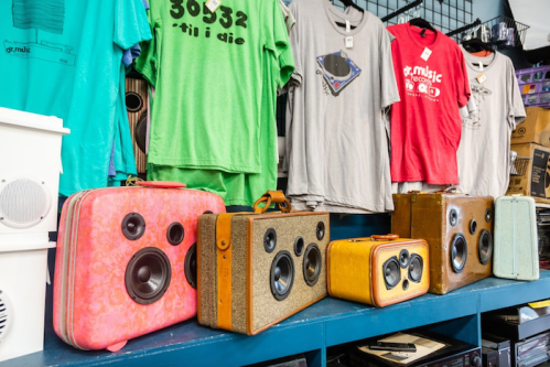A display of vintage speakers and colorful t-shirts in a shop, showcasing retro music-themed designs.