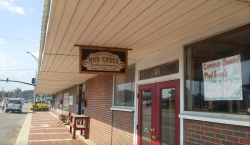 Sign for Mud Creek Trading Company on a storefront, with a brick facade and benches outside.