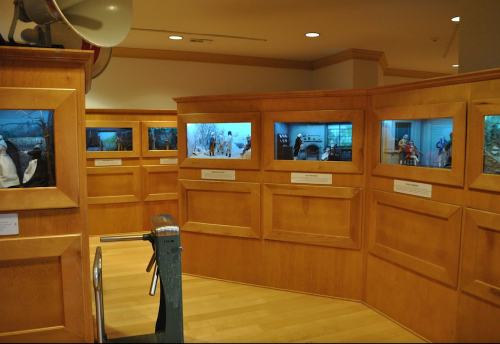 A wooden exhibit with illuminated displays showcasing various scenes in a museum setting.