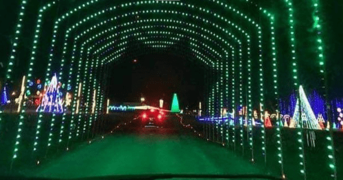 A car drives through a tunnel of green lights, surrounded by colorful holiday decorations.