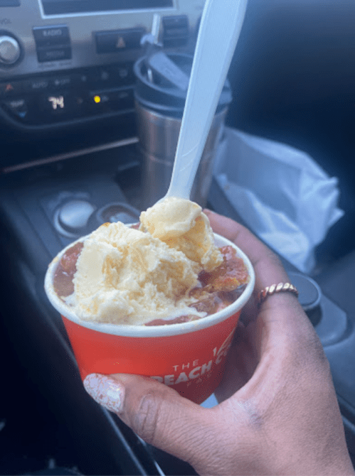 A hand holding a cup of dessert with ice cream on top, sitting in a car with a dashboard in the background.