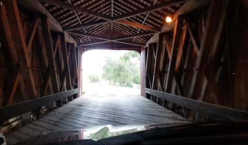 View from inside a covered bridge, looking out towards a tree-lined path.