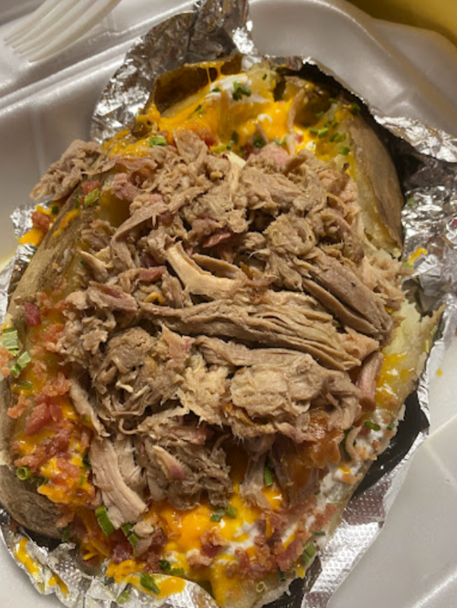 A loaded baked potato topped with shredded meat, cheese, bacon, and green onions, served in foil.