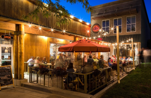 A lively outdoor dining area with string lights, people enjoying meals, and a cozy atmosphere at dusk.